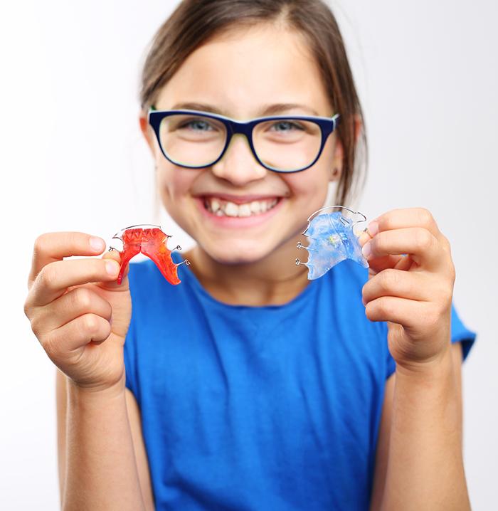 Young girl holding a red and a blue dentofacial orthopedic appliance